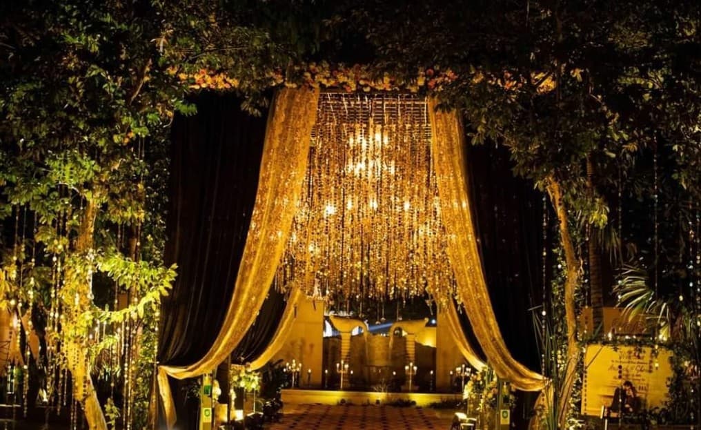 Golden draped wedding mandap entrance beneath string-light canopy