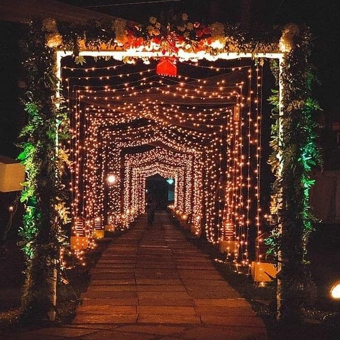 String-light tunnel walkway with floral canopy