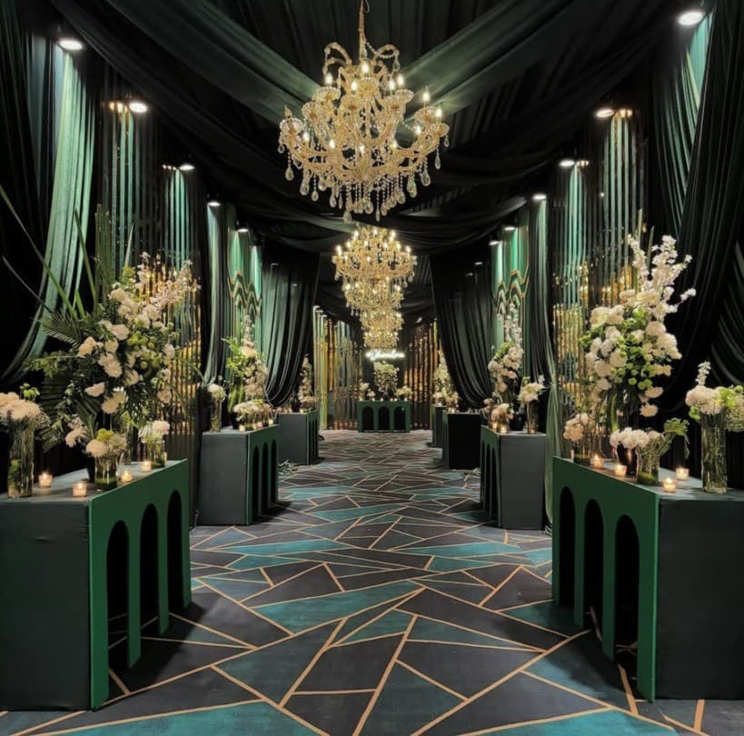 Emerald draped hallway with crystal chandeliers and floral tables